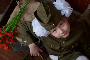 Zafer Günü 'nde 9 Mayıs' ta Sovyetler Birliği 'nin askeri üniformalı beyaz fiyonklu vatansever bir kız yanında fişekler ve mermiler olan tahta bir zeminde. Yakınlarda kırmızı karanfil çiçekleri var..