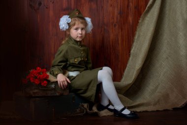 Zafer Günü 'nde 9 Mayıs' ta Sovyetler Birliği 'nin askeri üniformalı beyaz fiyonklu vatansever bir kız yanında fişekler ve mermiler olan tahta bir zeminde. Yakınlarda kırmızı karanfil çiçekleri var..