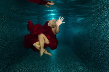 a beautiful girl in a red dress made of light fabric is resting after chemotherapy, red fabric, a bald girl in the pool after oncology treatment clipart