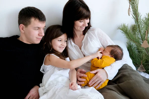 Fotoğrafta, dört kişilik sevgi dolu bir aile yatakta oturuyor. Annemin kucağında yeni doğmuş bir bebek var. aile aşkı.