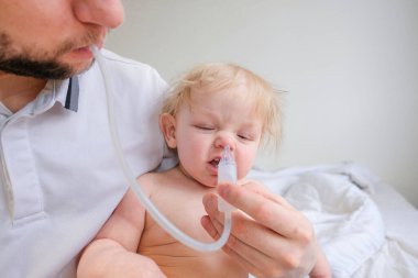 Beyaz bir odada babasının kucağında sümüklü bir çocuk oturuyor. Baba oğul gribi tedavi eder ve baba oğullarının burnunu sümükle temizler.