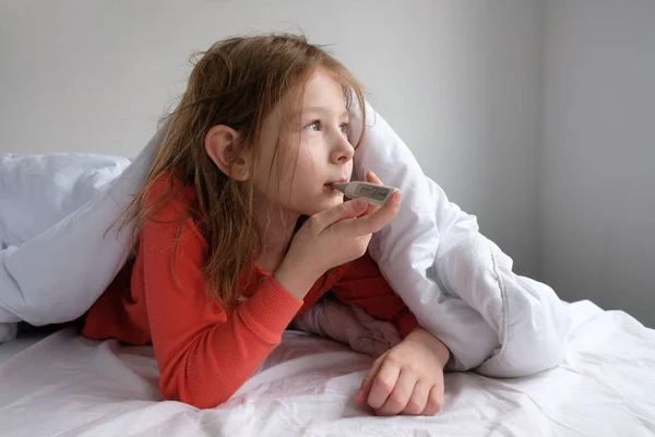 침대에 파자마를 소녀는 온도계를 가지고 독감에 걸렸을 경우의 온도를 측정하여 — 스톡 사진