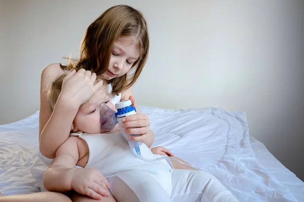 The children got sick. The older sister takes care of her brother and holds a gmu mask for inhalation. Medicine at home. stylish white room