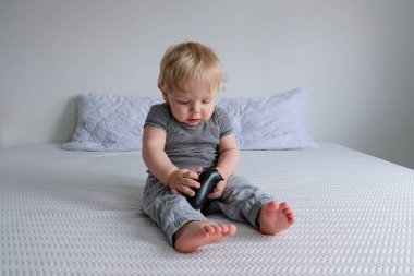 Yünlü elbiseli küçük bir çocuk beyaz bir yatakta oturur ve video oyunları oynar..