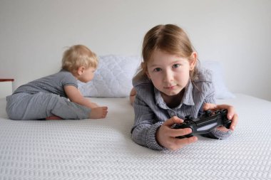 Kız ve oğlan izole bir şekilde beyaz bir yatakta oynuyorlar. Erkek ve kız kardeş, bir kız konsol ve video oyunu oynadığında eğlenir.