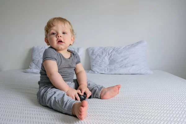 Niño Con Ropa Lana Sienta Una Cama Blanca Juega Videojuegos — Foto de Stock