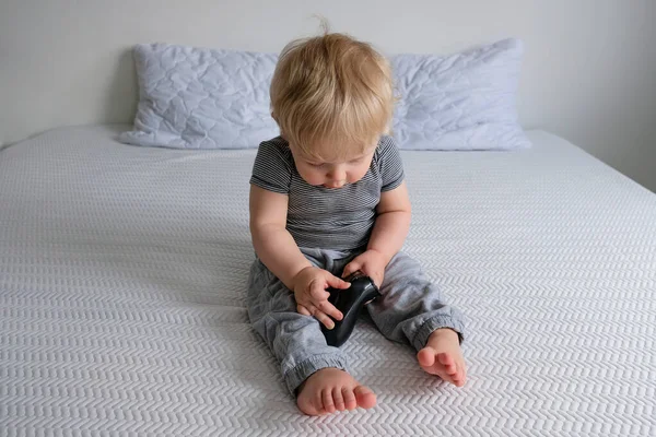 Niño Con Ropa Lana Sienta Una Cama Blanca Juega Videojuegos — Foto de Stock