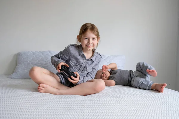 소녀와 소년은 집에서 침대에서 형제자매는 여자가 비디오 게임을 재미있게 수있다 — 스톡 사진