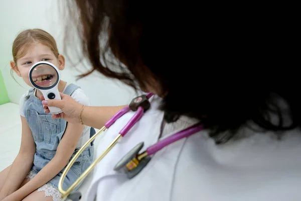 Doktorun ofisinde boğazı ağrıyan kızların acil muayenesi. Doktor kızın ağzına bakar bademciklerine, diline ve dişlerine.
