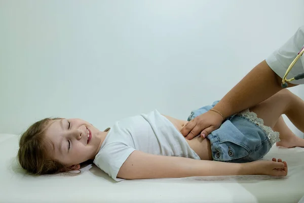 Doktor çocuk doktoru kanepede yatan bir çocuğun midesini kontrol eder. Cerrah, kızın midesini hastane odasında sarıyor.