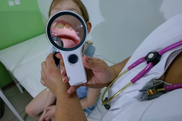 Doktorun ofisinde boğazı ağrıyan kızların acil muayenesi. Doktor kızın ağzına bakar bademciklerine, diline ve dişlerine.