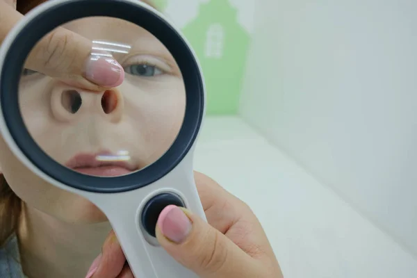 Çocuk kliniğinde elinde büyüteçle bir çocuk. Modern otoskop kızın burnunu incelemek için yakın plan doktor eli. Çocuk sağlığı ve hastalıkların önlenmesi