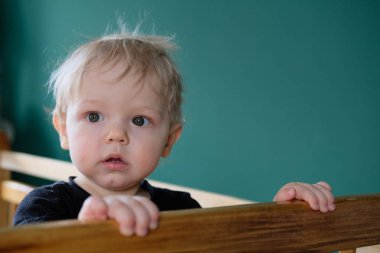 Sarı saçlı çocuk uyandı ve bir şey onu şaşırttı. Beşikte duran bir bebeğin yakın plan portresi. Çocuk çok memnun ve mutlu..