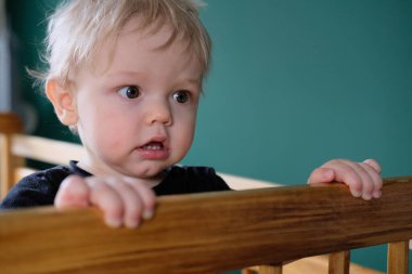 Sarı saçlı çocuk uyandı ve bir şey onu şaşırttı. Beşikte duran bir bebeğin yakın plan portresi. Çocuk çok memnun ve mutlu..