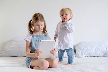 Evde yataktaki iki çocuk iş adamlarıyla oynuyorlar. Küçük bir kız kardeşiyle tabletle oynuyor..
