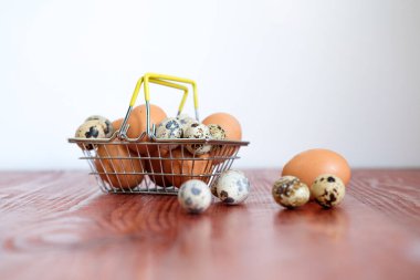 bıldırcın ve tavuk yumurtalarının bulunduğu market sepeti ahşap bir masada duruyor.