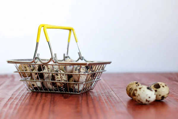 supermarket grocery basket with quail and chicken eggs stands on a wooden table