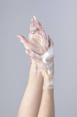 Beyazların elleri, yeşil köpüklü Marsilya sabunu ile birbirlerini yıkıyor. Gri arka planda, yapıcı ışıklar ve gölgelerle izole edilmiş.