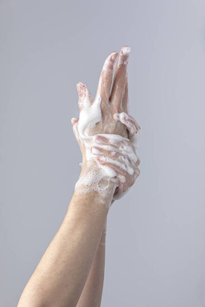 White people's hands washing each other with green foamy Marseille's soap isolated in front of a grey background with structurant lights and shadows