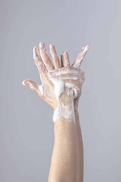 White people's hands washing each other with green foamy Marseille's soap isolated in front of a grey background with structurant lights and shadows