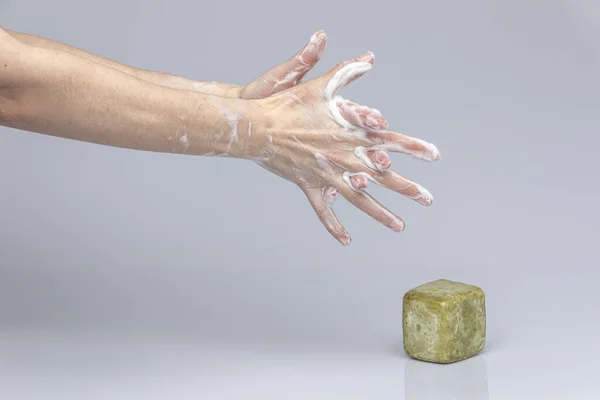 Stock image White people's hands washing each other with green foamy Marseille's soap isolated in front of a grey background with structurant lights and shadows