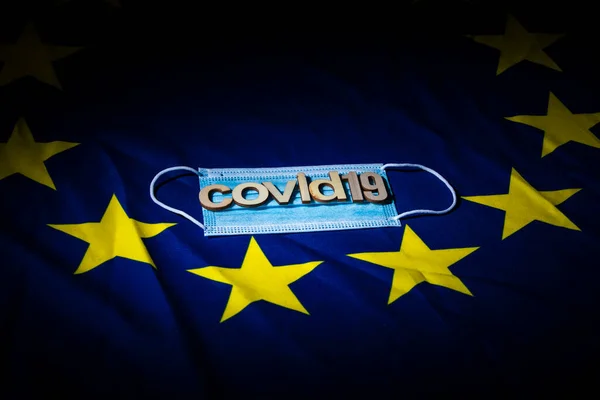 flat face mask on a European flag with wooden letters forming words to create a concept