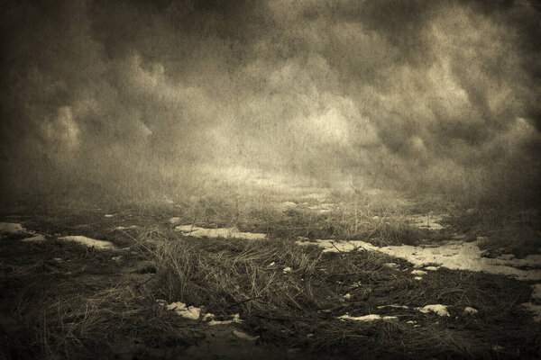 Грязное поле с сухой травой и следами снега, дымовое облако на заднем плане
.