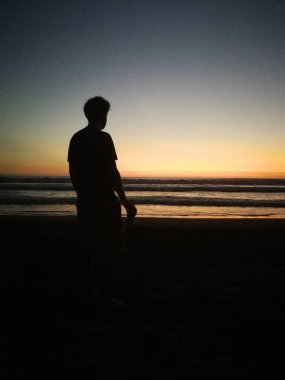 Sahilde gün batımlı bir adamın silueti.