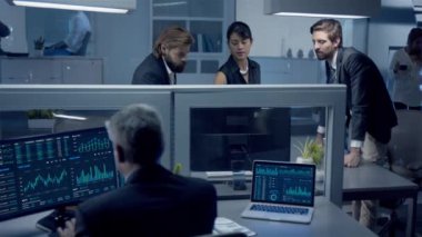 Gece geç saatlere kadar çalışan çeşitli profesyoneller bilgisayardaki hisse senedi verilerini tartışıyor masasında oturan orta yaşlı çalışanlar Masaüstü ve dizüstü bilgisayar kullanıyor..