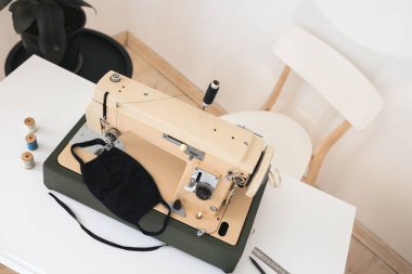 Bej dikiş makinesi evde koruyucu bir tıbbi maske dikme süreci pastel açık renklerde elde yapılır.