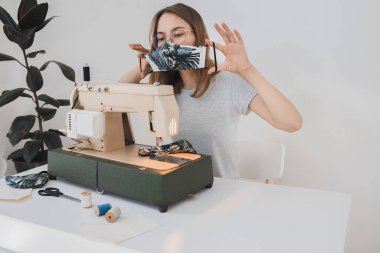 Gribi önlemek için evdeki dikiş makinesine koruyucu ilaç maskesi takan bir kız. Covid-19 beyaz arka planı olan odada.