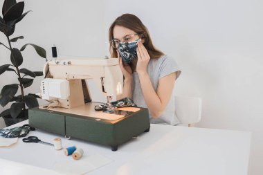 Gribi önlemek için evdeki dikiş makinesine koruyucu ilaç maskesi takan bir kız. Covid-19 beyaz arka planı olan odada.