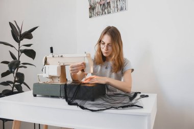 El yapımı bir hobide, eski bir dikiş makinesinin üzerinde siyah kumaştan yapılmış dikiş elbisesi diken kız.