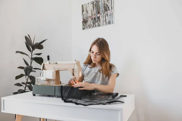 The girl Sewing dress made of black fabric tulle on a vintage sewing machine in the room workplace handmade Hobby