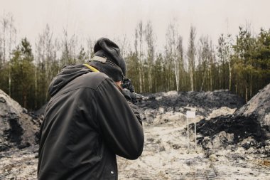 Adamın biri çölde atış poligonunda av tüfeğiyle ateş ediyor.