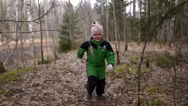 녹색 점프수트를 입은 금발의 소녀가 봄 전에 뛰어다니고 많은 나무들이 있어요 — 비디오