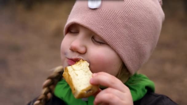 Retrato de una chica en un sombrero rosa comiendo un bollo crujiente en la naturaleza en el bosque — Vídeos de Stock