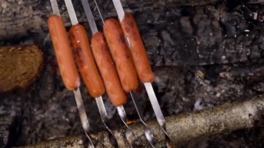 Bir sosisli sandviç şiş üzerinde ateşte kızarır. Barbekü için.