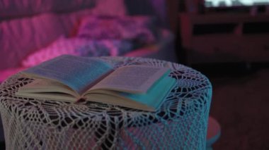 Kitap renkli bir ışıkta masanın üzerinde yatıyor. Arkasında çalışmayan bir televizyon var. Çerçeve yaklaşıyor, günlük iyileşiyor ve plana göre büyüyor.