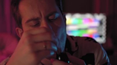 Bir adamın pipo içerken yakın plan fotoğrafı. Bıyıklı ve inekli bir adam. Oda renkli, pembe ve mavi renkli. Masadaki bir taburede oturuyor.