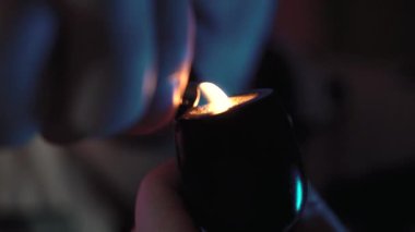 Bir adamın pipo içtiği yakın plan. Bıyıklı ve inekli bir adam. Oda renkli, pembe ve mavi renkli. Masadaki bir taburede oturuyor.