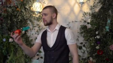 Vahşi adam yerden ısırılmış kırmızı bir elma aldı ve arkasından fırlattı, üzgün, endişeli. Yeşilliğin arka planında, takım elbiseli bir adam korkar, endişelenir.