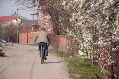 Köyün arka tarafında bisiklet süren yaşlı bir adam.
