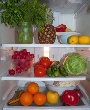 Taze çiğ meyve ve sebzelerle dolu buzdolabı, çam elması, maydanoz, dereotu, limon, biber, portakal, elma, muz, yeşil lahana, salatalık, kırmızı domates, turp, zencefil