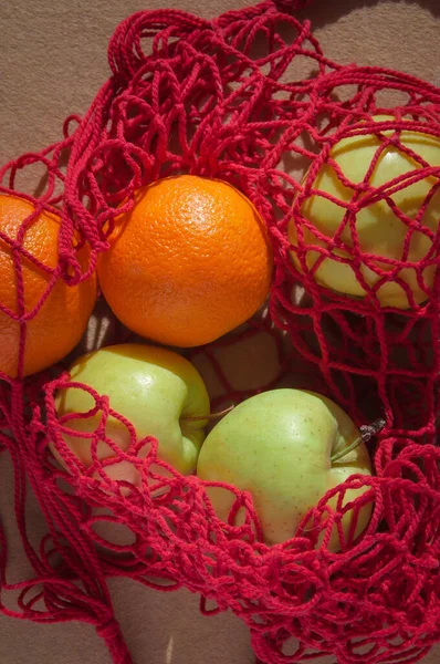red string bag with oranges and green apples with fruits