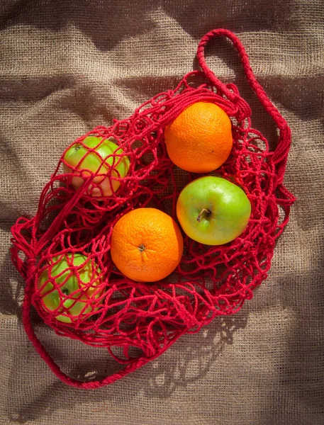 red string bag with oranges and green apples with fruits