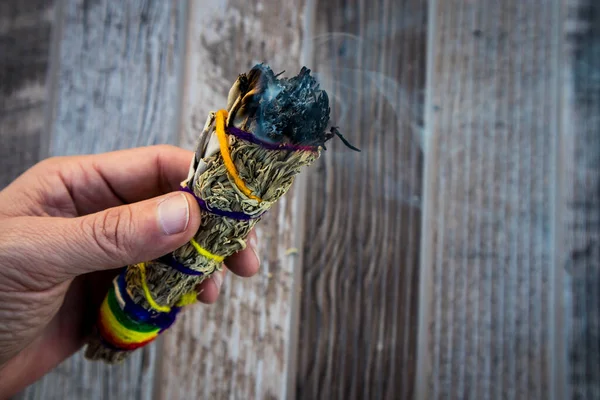 Hand holding bundle of burning sage against wood background