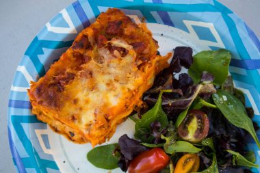 Lazanya ve tek kullanımlık kağıt tabakta yeşil salata.