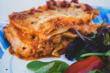 Lazanya ve tek kullanımlık kağıt tabakta yeşil salata.