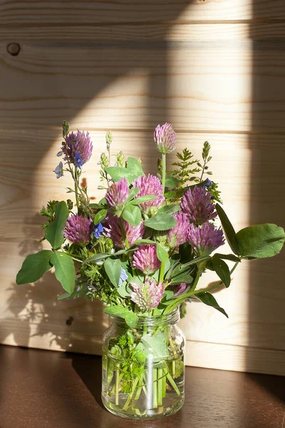 Bunch of red clover flowers close up. Spring red or pink clover flowers bouquet on white wooden table background, top view. Purple red wild clover flowers from field, text space